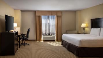 A hotel room with a bed, desk, chair, television, and a window with curtains.