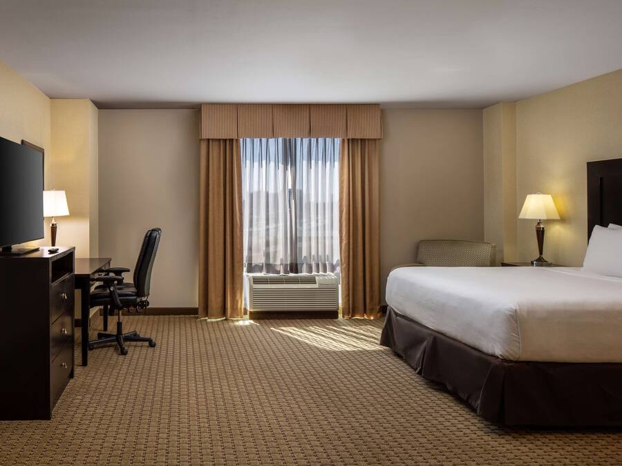 Une chambre d’hôtel équipée d’un lit, d’un bureau, d’une chaise, d’une télévision et d’une fenêtre avec des rideaux.