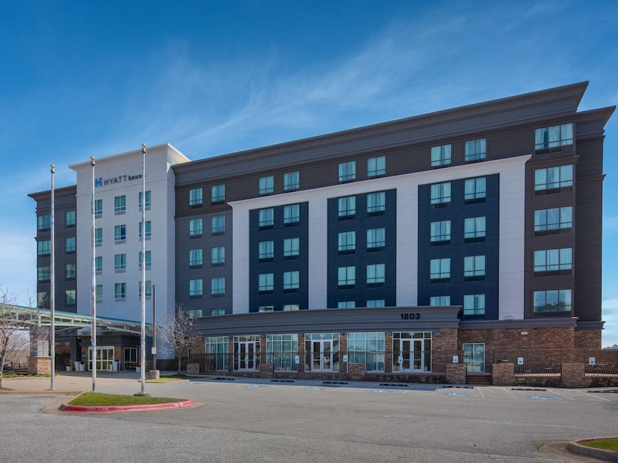 A modern hotel with a glass entrance, multiple floors, and a clear sky.