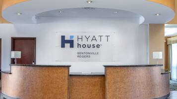Mostrador de recepción de Hyatt House con diseño moderno, un cartel grande encima y una puerta a la izquierda.