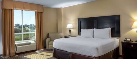 A hotel room with a large bed, a chair, a desk, and a window with curtains.