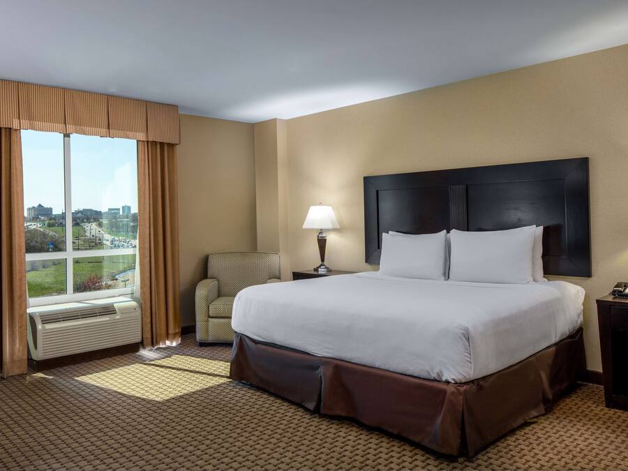 A hotel room with a large bed, a chair, a desk, and a window with curtains.