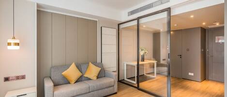 A modern living room with a grey sofa, wooden flooring, and a glass partition.