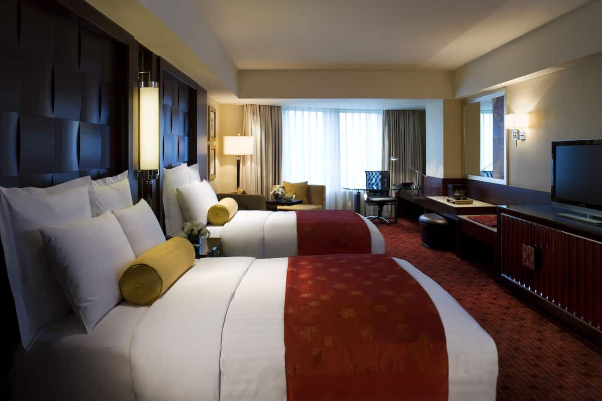 A hotel room with two large beds, a desk, a television, and a window with curtains.