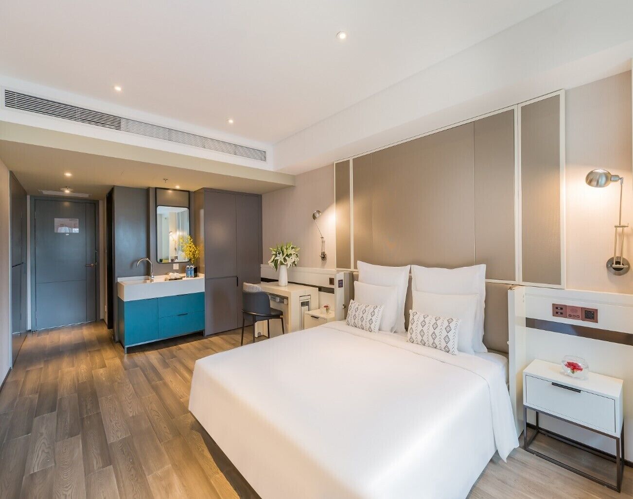 A modern hotel room with a large bed, a desk, a vanity, and a walk-in closet.