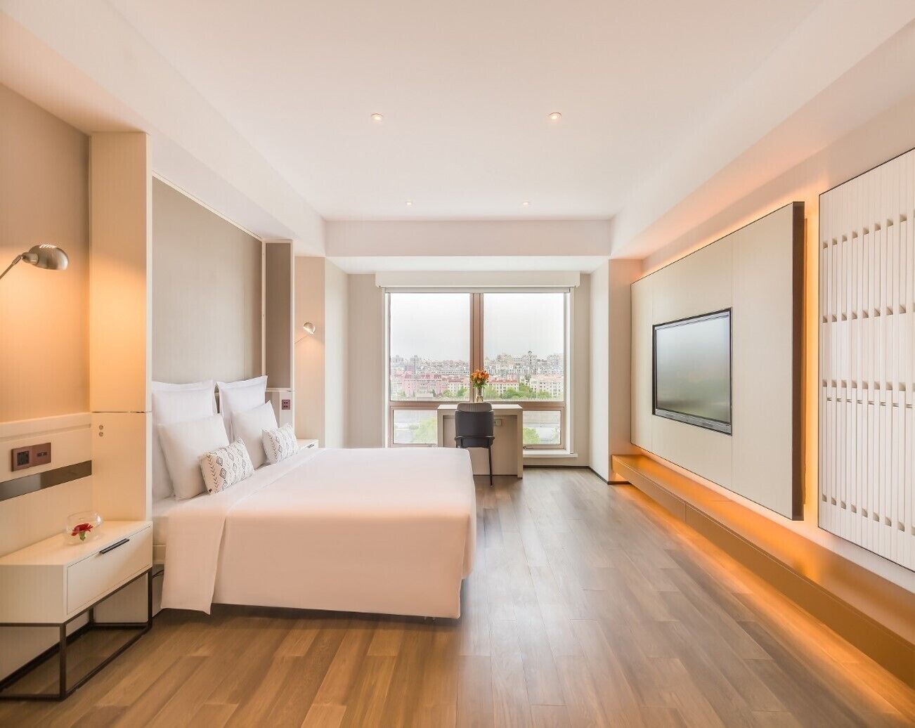 Ein modernes Hotelzimmer mit einem großen Bett, einem Schreibtisch, einem Fernseher und Blick auf die Stadt.