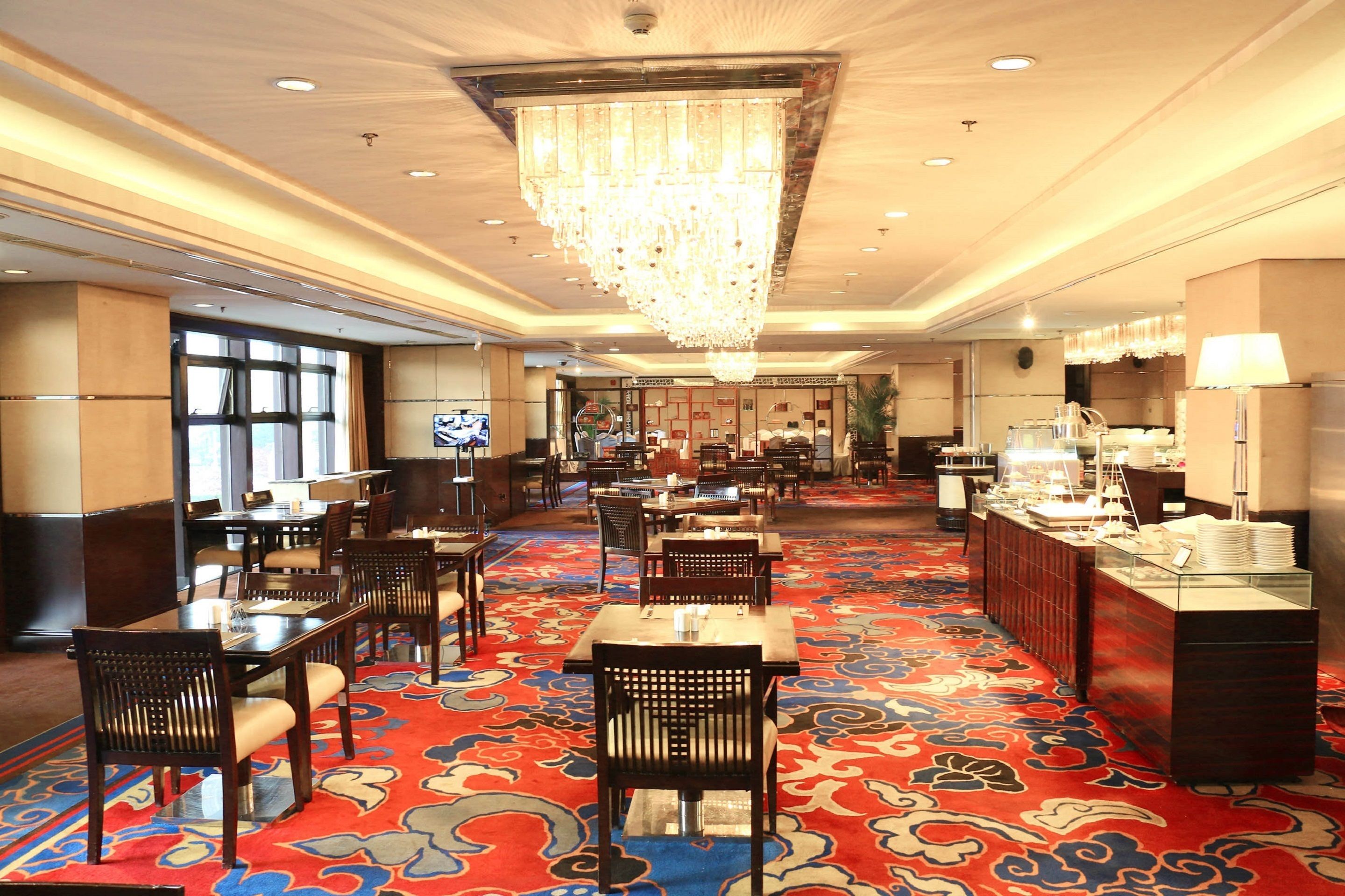 Un hall d’hôtel doté d’un grand lustre, d’un espace buffet et d’un tapis à motifs.