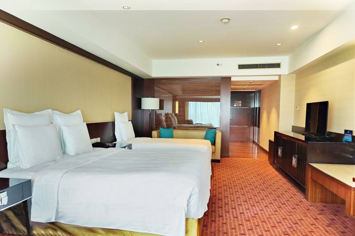 A hotel room with a large bed, a desk, a television, and a seating area with a lamp.