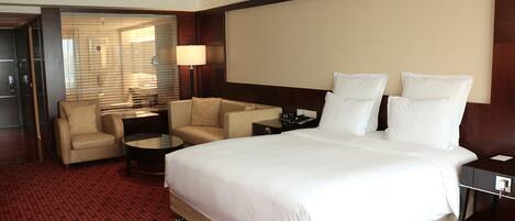 A hotel room with a large bed, two armchairs, a small table, and a TV screen.