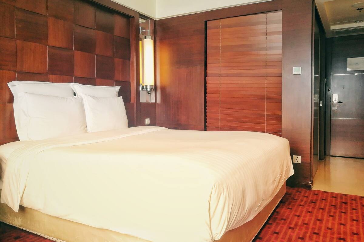A hotel room with a large bed, wooden headboard, and a red patterned carpet.