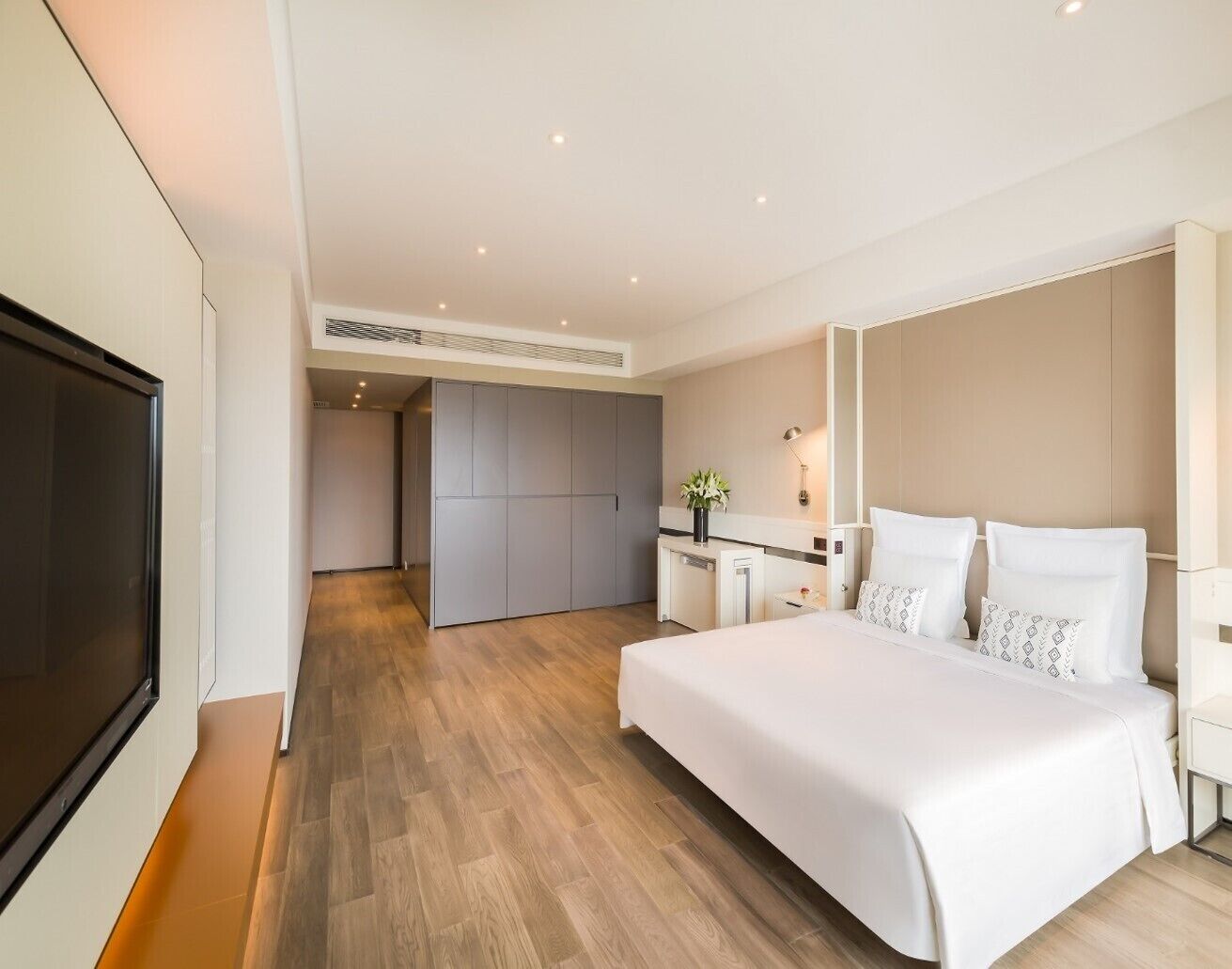 A modern hotel room with a large bed, a desk, and a TV.