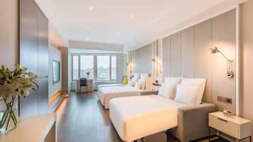 A modern hotel room with two beds, a desk, and a view of the city.