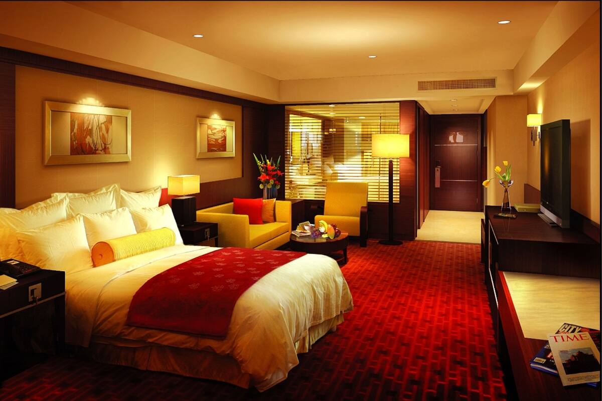 A hotel room with a large bed, a sofa, a TV, and a desk with a lamp.