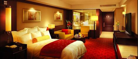 A hotel room with a large bed, a sofa, a TV, and a desk with a lamp.