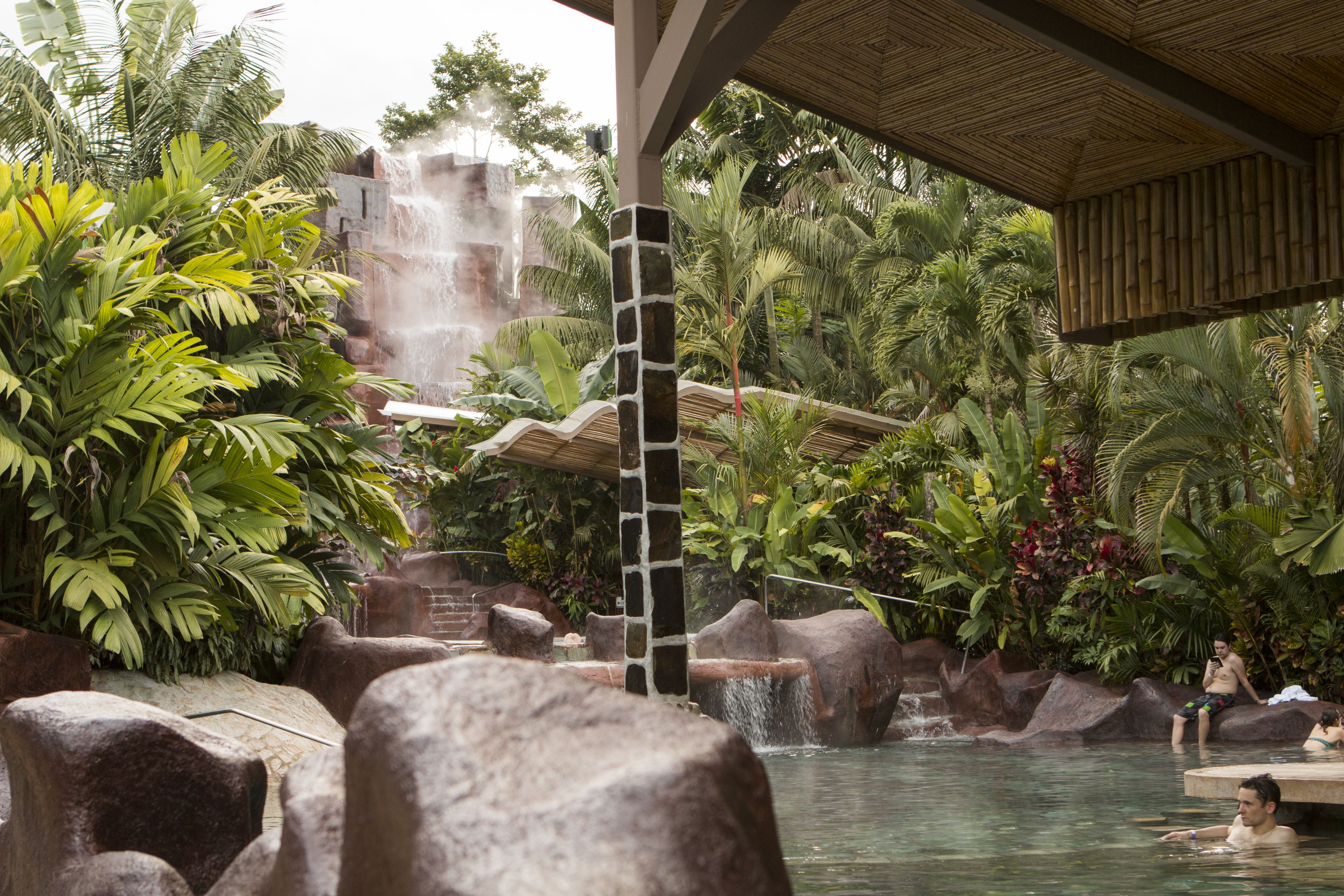 Un resort tropical con una cascada, formaciones rocosas y exuberante vegetación.