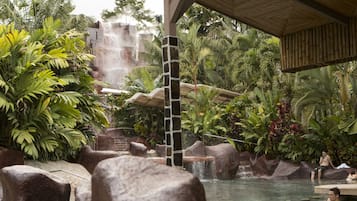 Un resort tropical con una cascada, formaciones rocosas y exuberante vegetación.