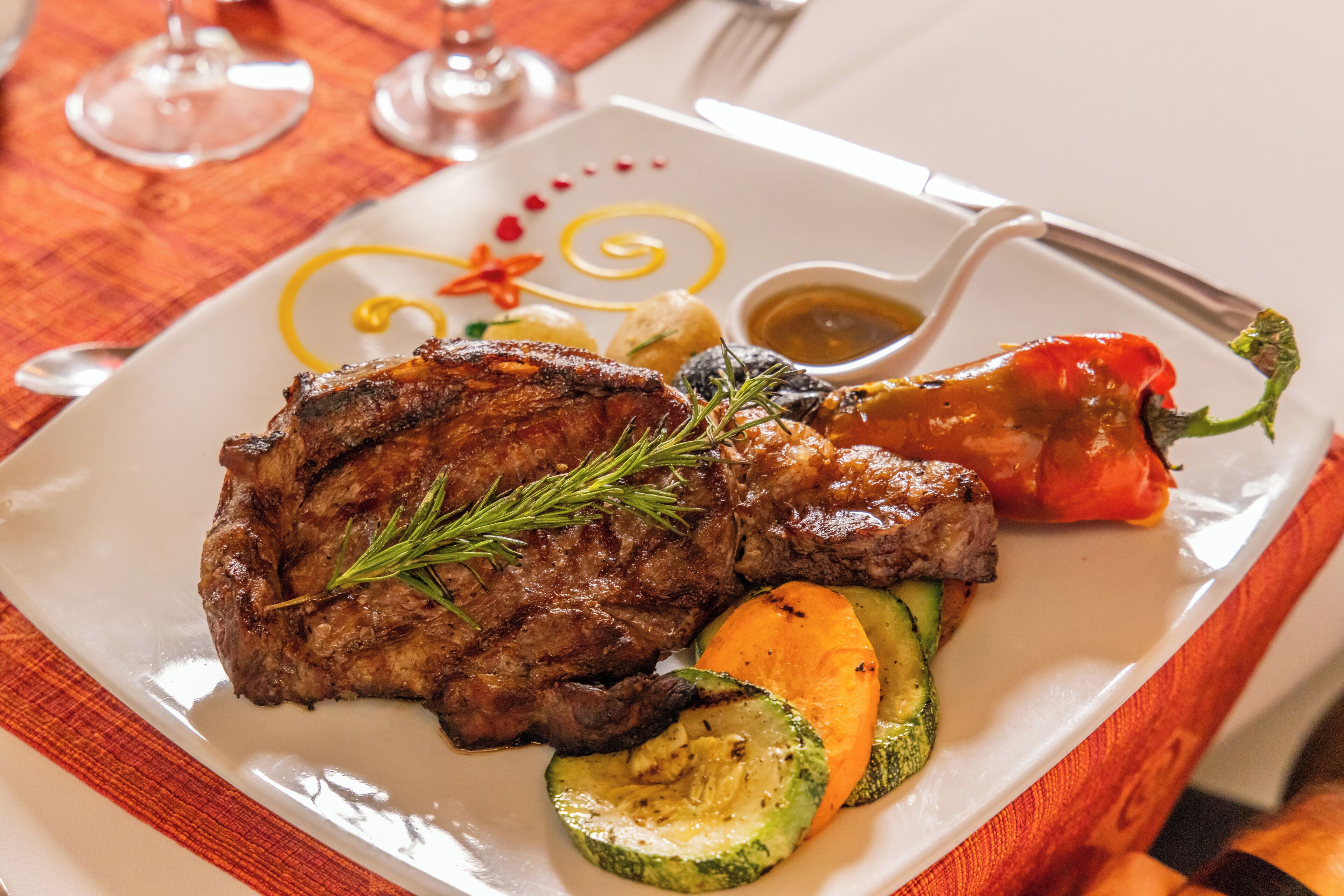 A plate of food with a steak, vegetables, and a red pepper.