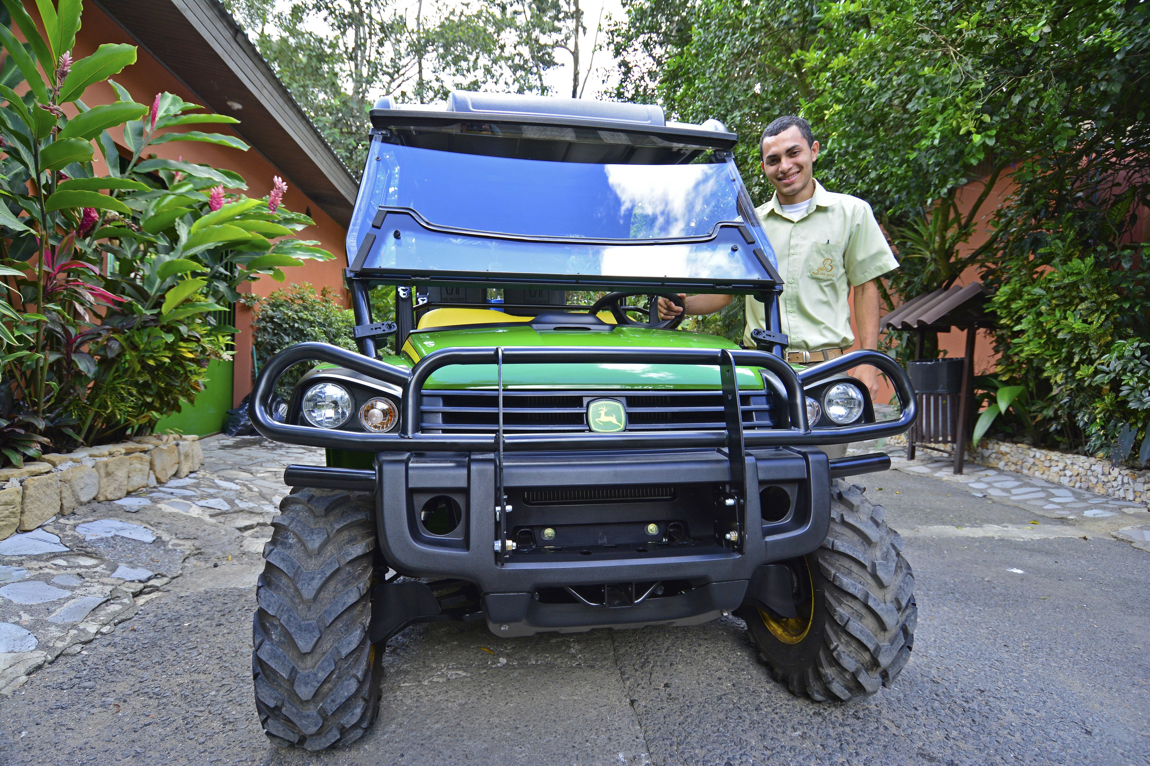 A green and blue utility vehicle parked in front of a building with stone steps and lush greenery.