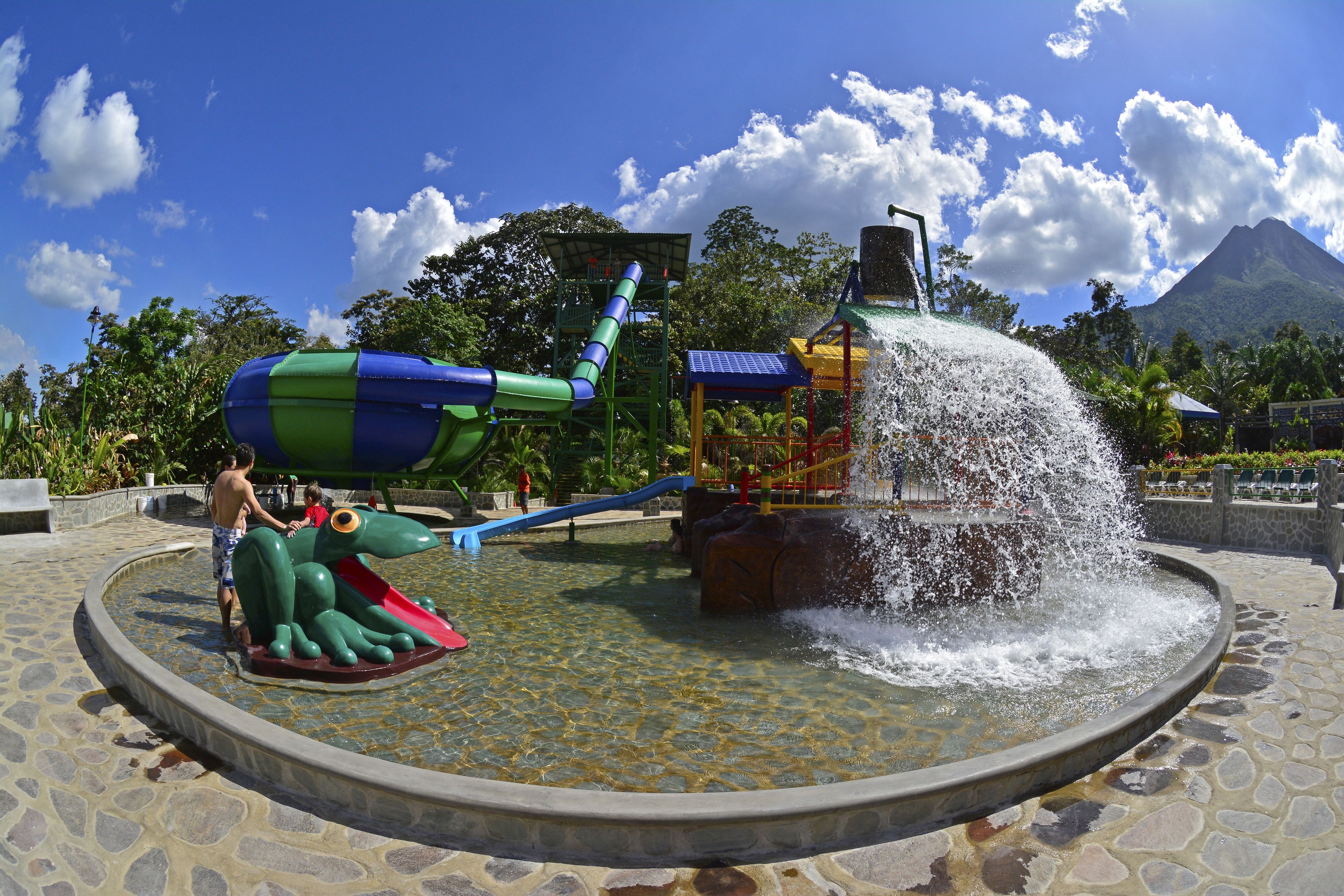 Un parc aquatique avec un toboggan, une fontaine et une montagne en arrière-plan.
