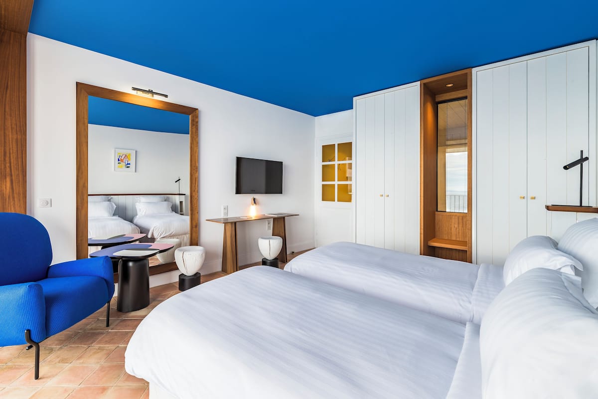 Habitación de hotel con dos camas, un escritorio, una silla, un televisor y un armario.