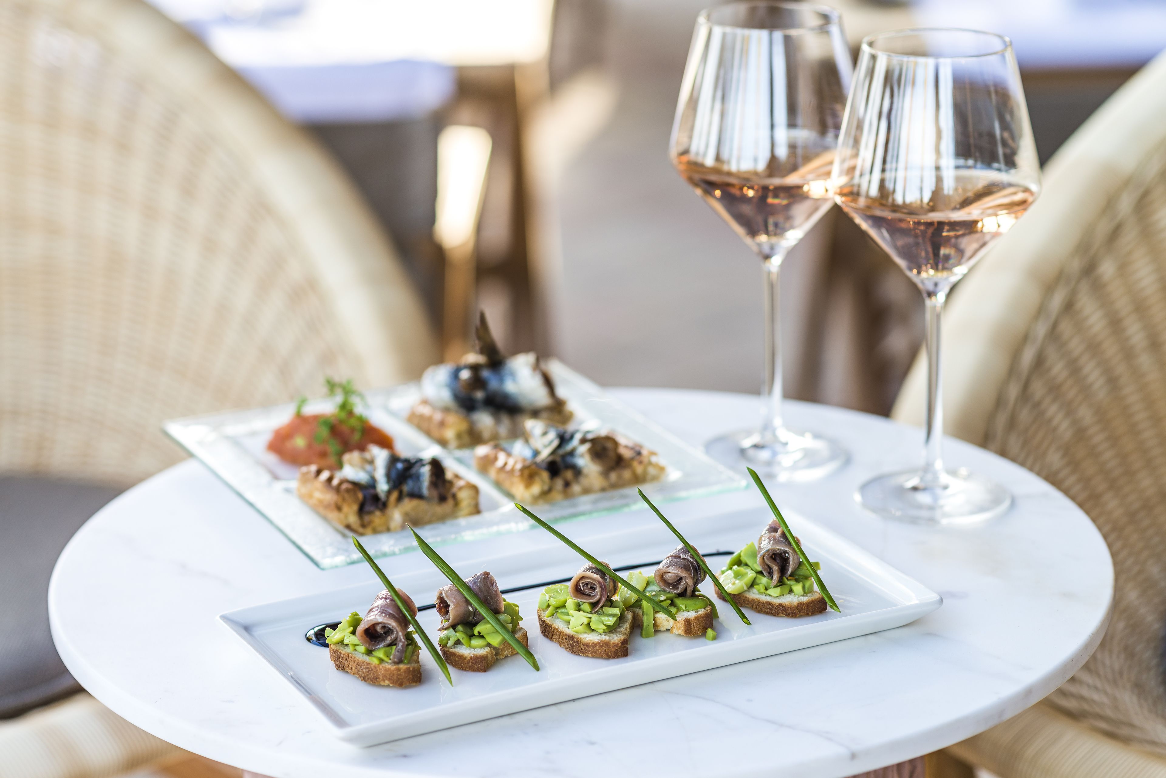 A table with a white marble top, displaying appetizers and two glasses of rosé wine.