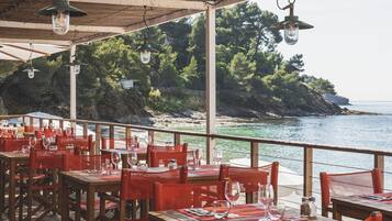 Een restaurant aan zee met tafels en stoelen, met uitzicht op de oceaan.