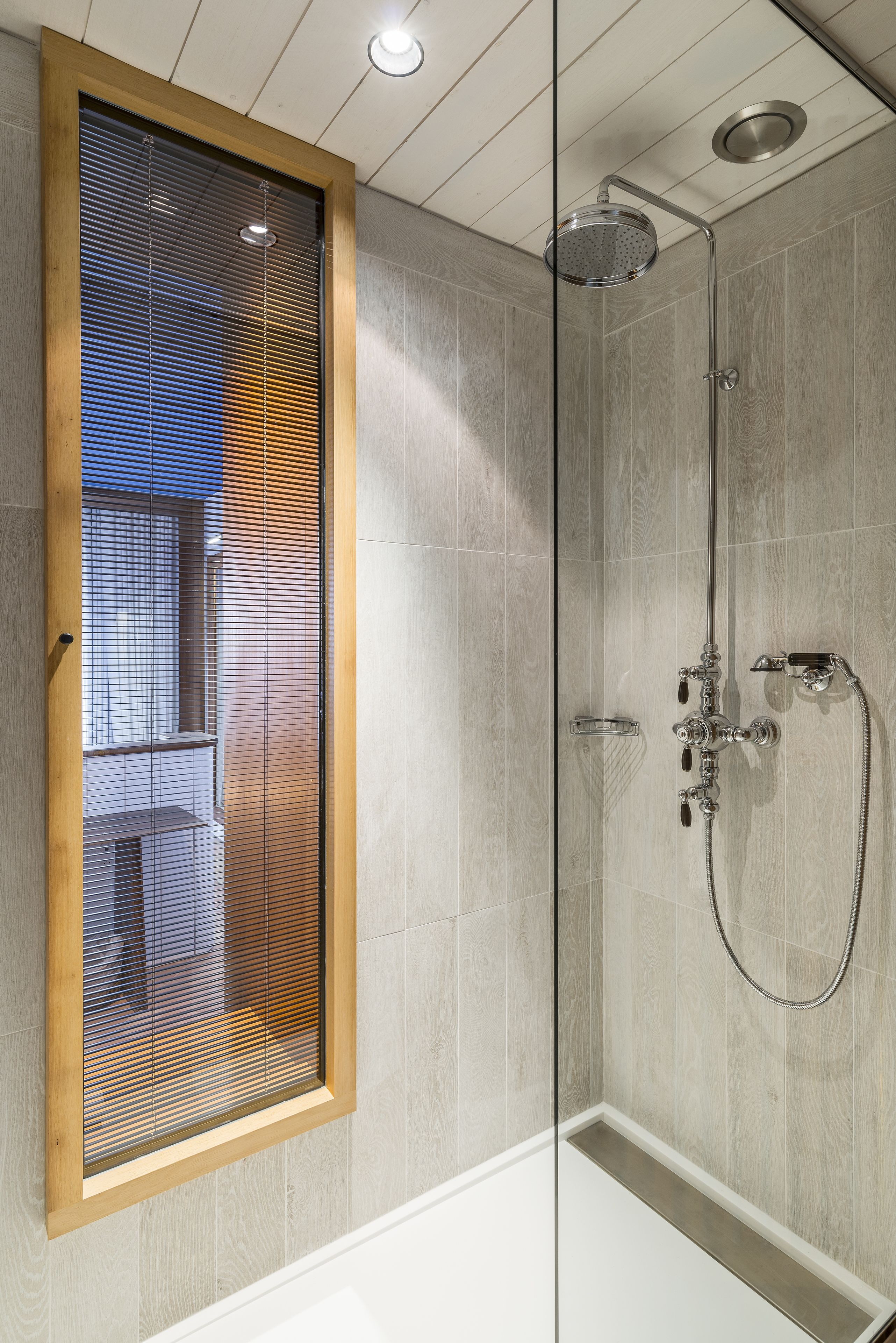 A modern shower with a glass door, a wooden-framed window, and a visible showerhead.
