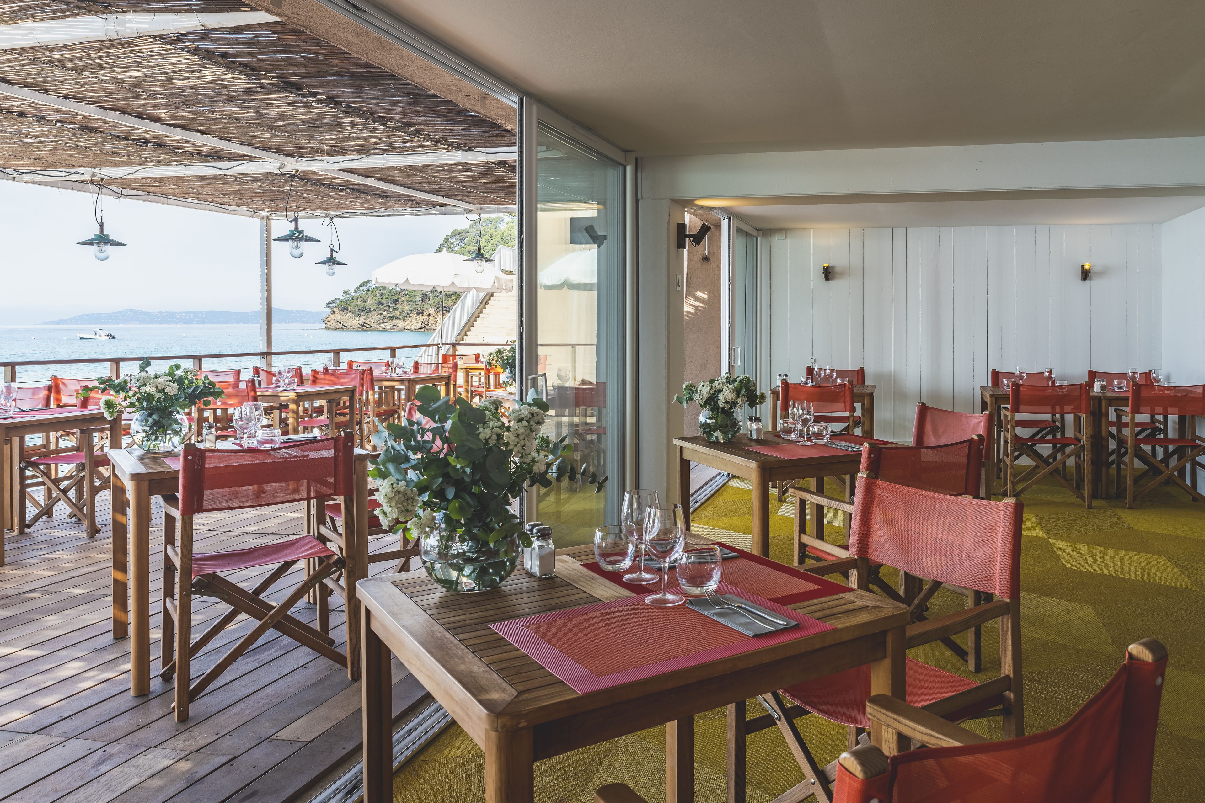 Un restaurante con mesas de madera y sillas rojas, frente a una vista del mar.