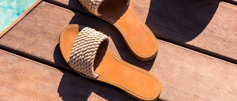 A pair of woven sandals and a straw hat on a wooden table by a pool.
