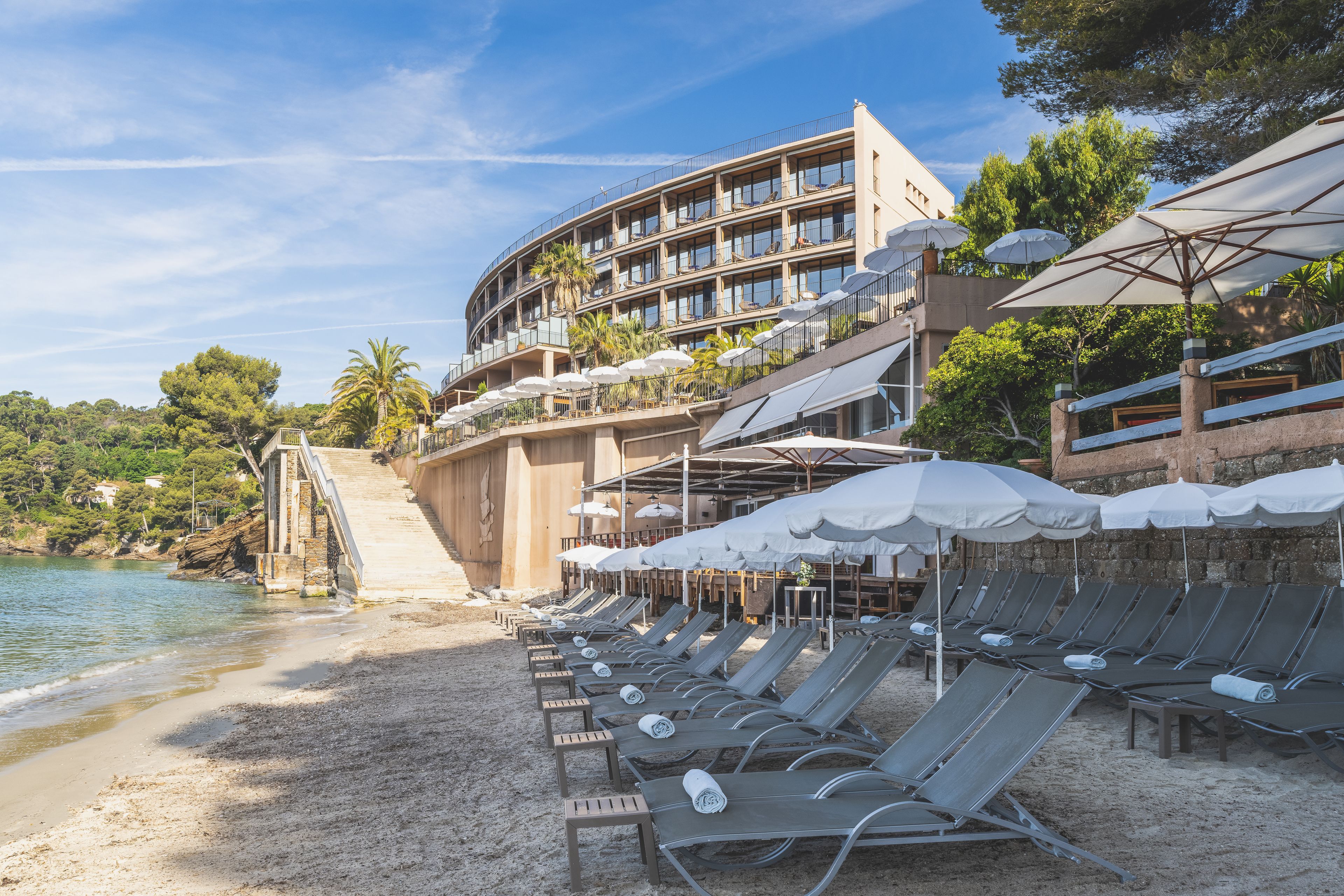 Un hôtel situé en bord de mer, doté de chaises longues, de parasols et d’un espace piscine.