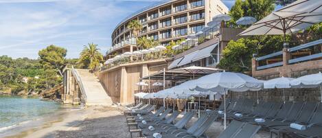 Un hôtel situé en bord de mer, doté de chaises longues, de parasols et d’un espace piscine.