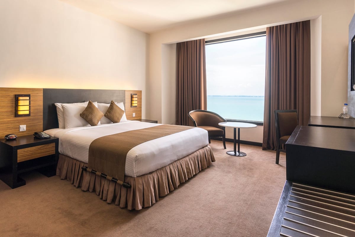A hotel room with a large bed, a desk, a chair, a small table, and a view of the sea.