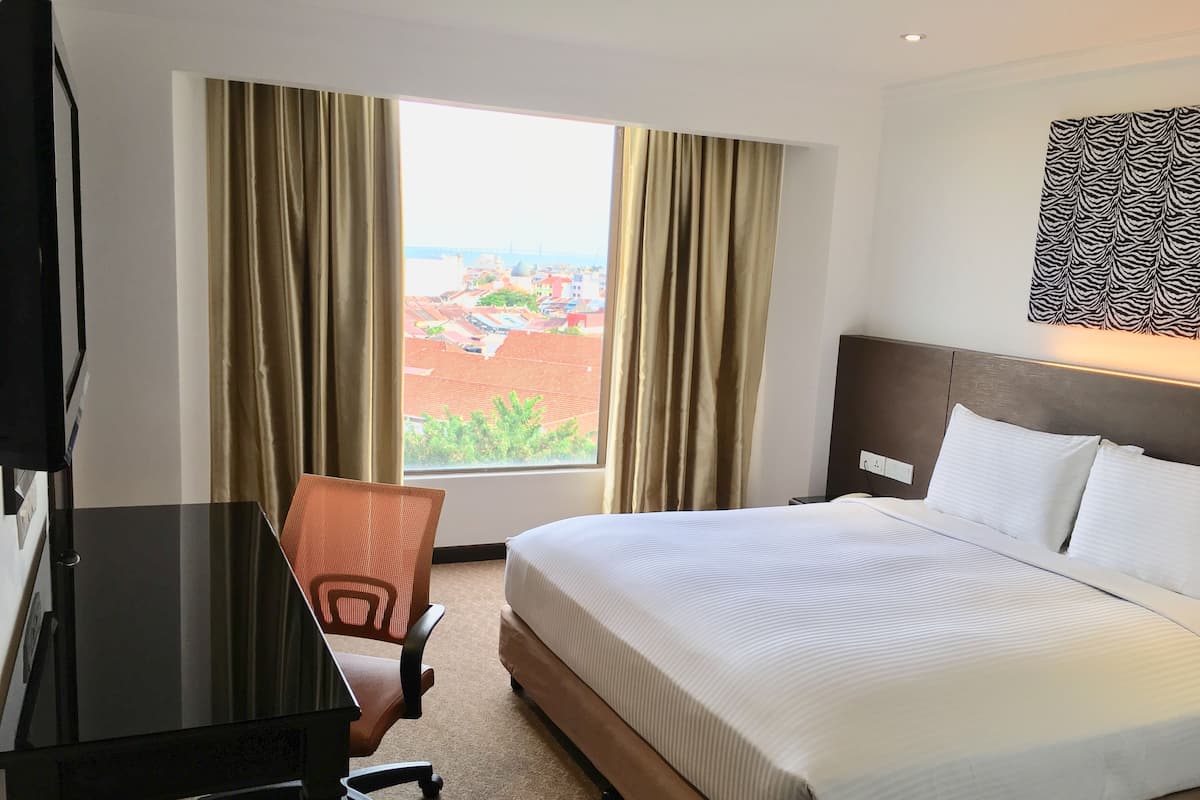 A hotel room with a bed, a desk, a chair, and a large window with curtains.