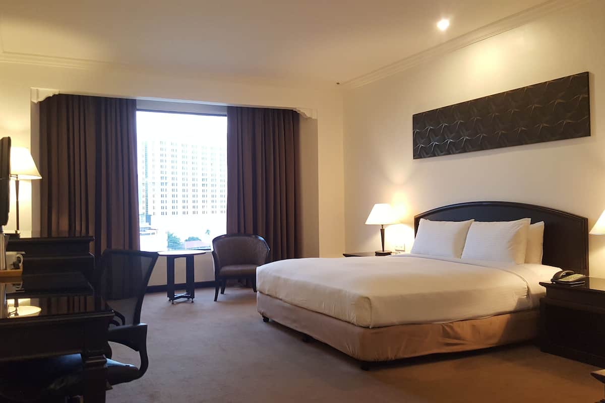 A hotel room with a bed, desk, chair, and a large window with curtains.