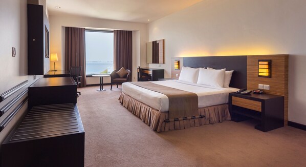 A hotel room with a bed, bedside table, lamp, chair, desk, and a view of the outdoors. - Bayview Hotel Georgetown Penang (George Town)