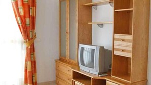 A room with a wooden wardrobe, a television on top, and a curtain. - Apartamentos Ambar Beach (Calpe)