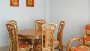 A dining area with a round wooden table and six wicker chairs. - Apartamentos Ambar Beach (Calpe)