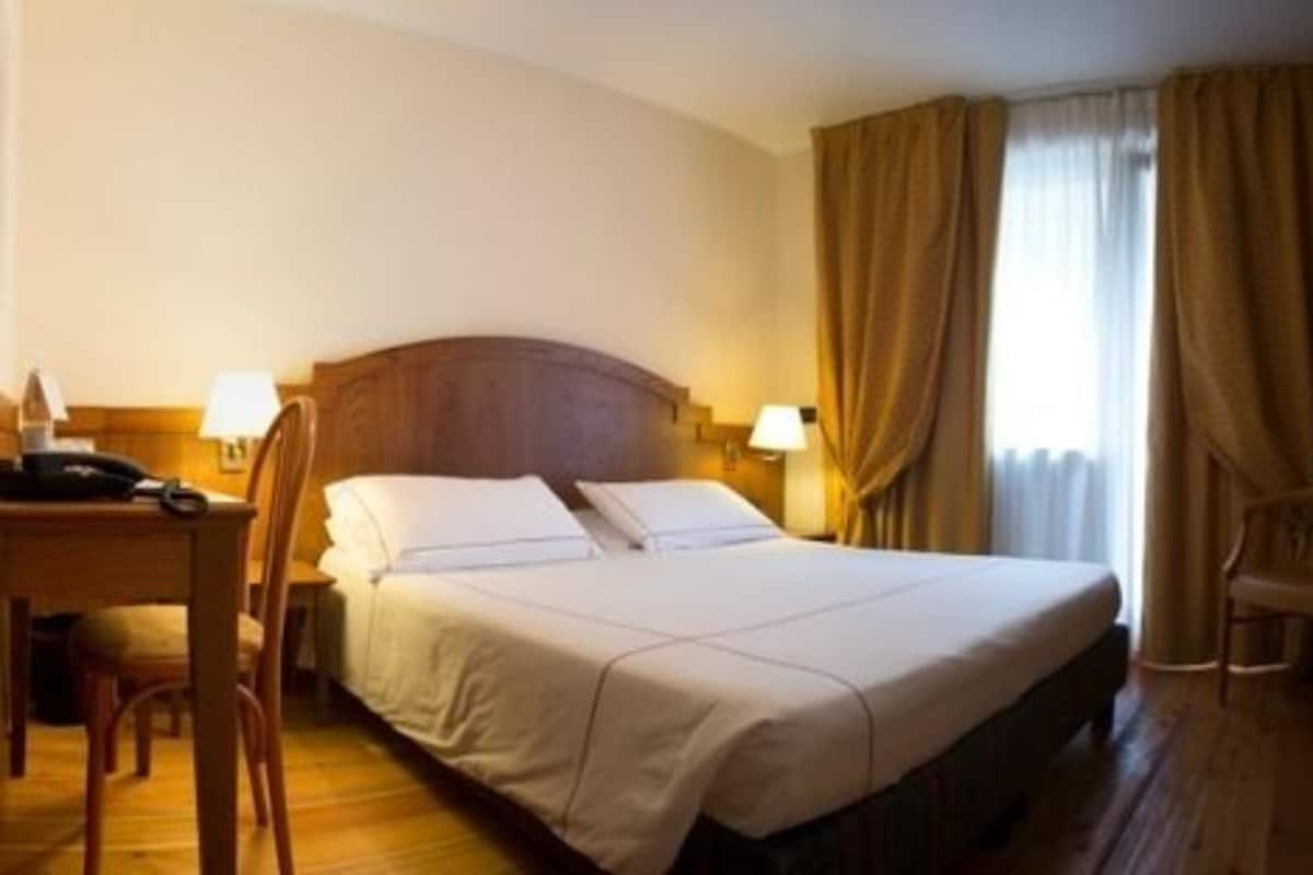 Hotellihuone, jossa on sänky, yöpöytälamput, kirjoituspöytä puhelimineen ja tuoli.