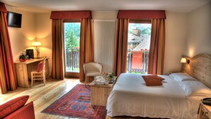 Habitación de hotel con cama, escritorio, silla, televisor y ventana con cortinas.