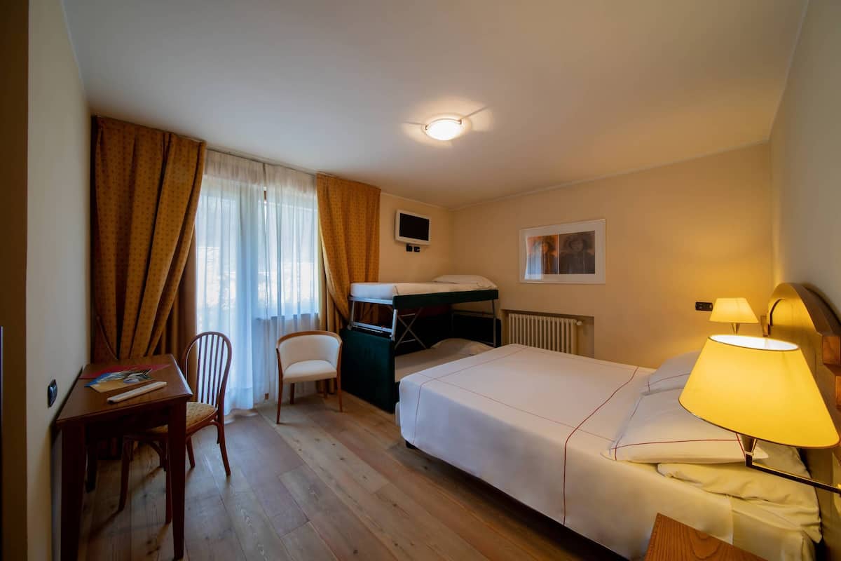 Hotellihuone, jossa on yksi sänky, työpöytä tuolilla, pieni pöytä, televisio ja ikkuna, jossa on verhot.