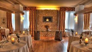 Un comedor con mesas redondas, velas y una pared de piedra con chimenea.