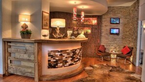 Un área de bar moderna con mostrador de madera, pared de piedra y dos sillas cómodas.