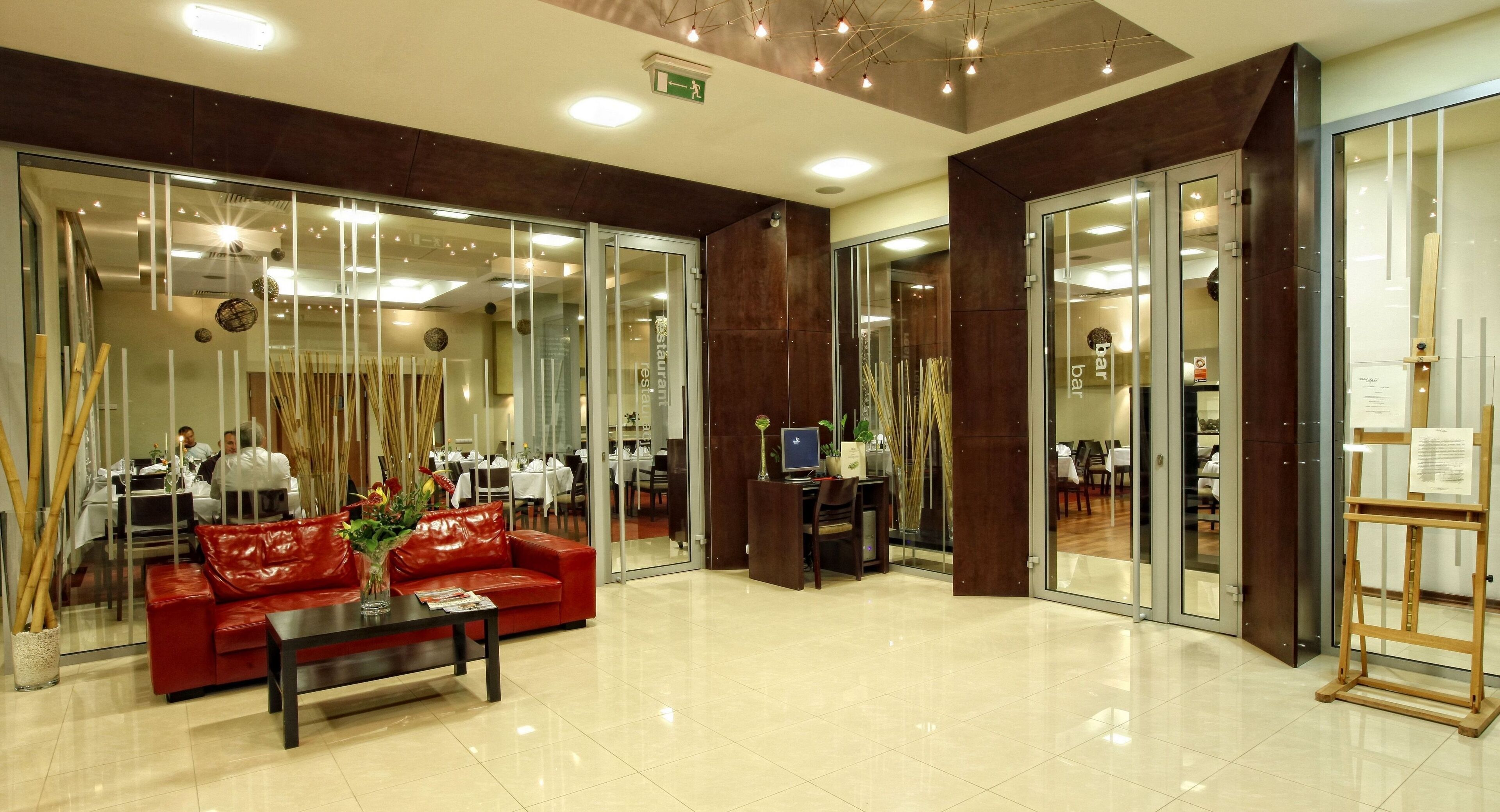 A modern hotel lobby with a red leather sofa, a coffee table, and a reception desk.