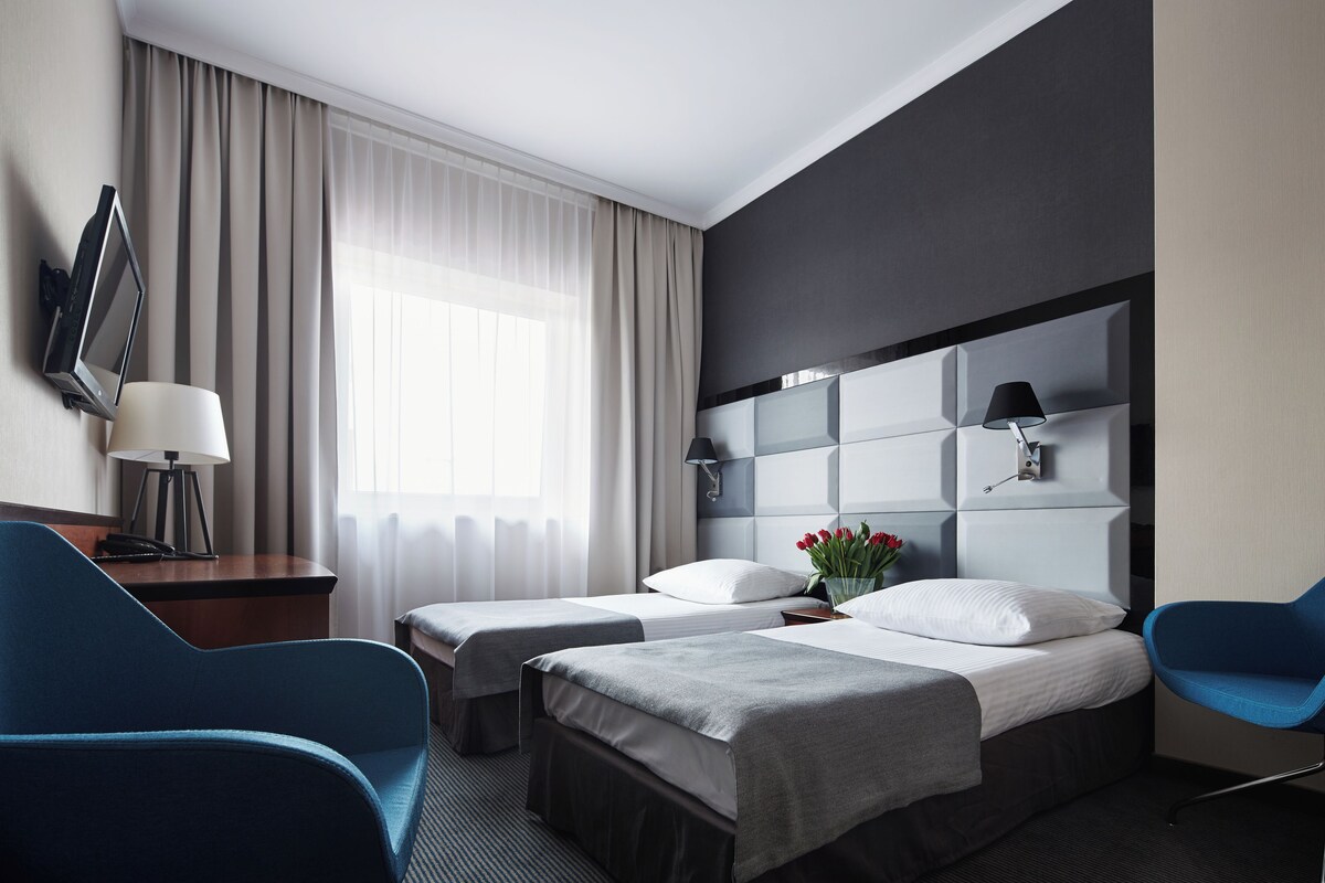 Habitación de hotel con dos camas, un escritorio, una silla, un televisor y una ventana con cortinas.
