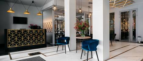 A modern hotel lobby with a geometric patterned reception desk, blue chairs, and contemporary lighting fixtures.