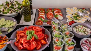 Variedad de alimentos, incluyendo tomates en rodajas, una ensalada y varios recipientes de vidrio pequeños con ensaladas en capas.