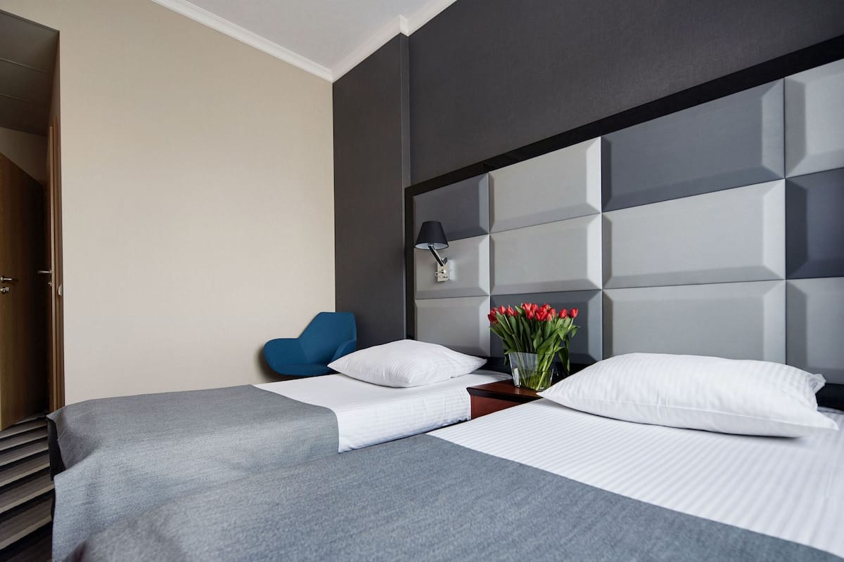 Moderni hotellihuone, jossa on suuri sänky, yöpöytä, lamppu ja maljakko, jossa on kukkia.