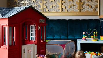 Um espaço de brincadeiras com uma casinha vermelha, um ábaco e diversos brinquedos espalhados pelo chão.