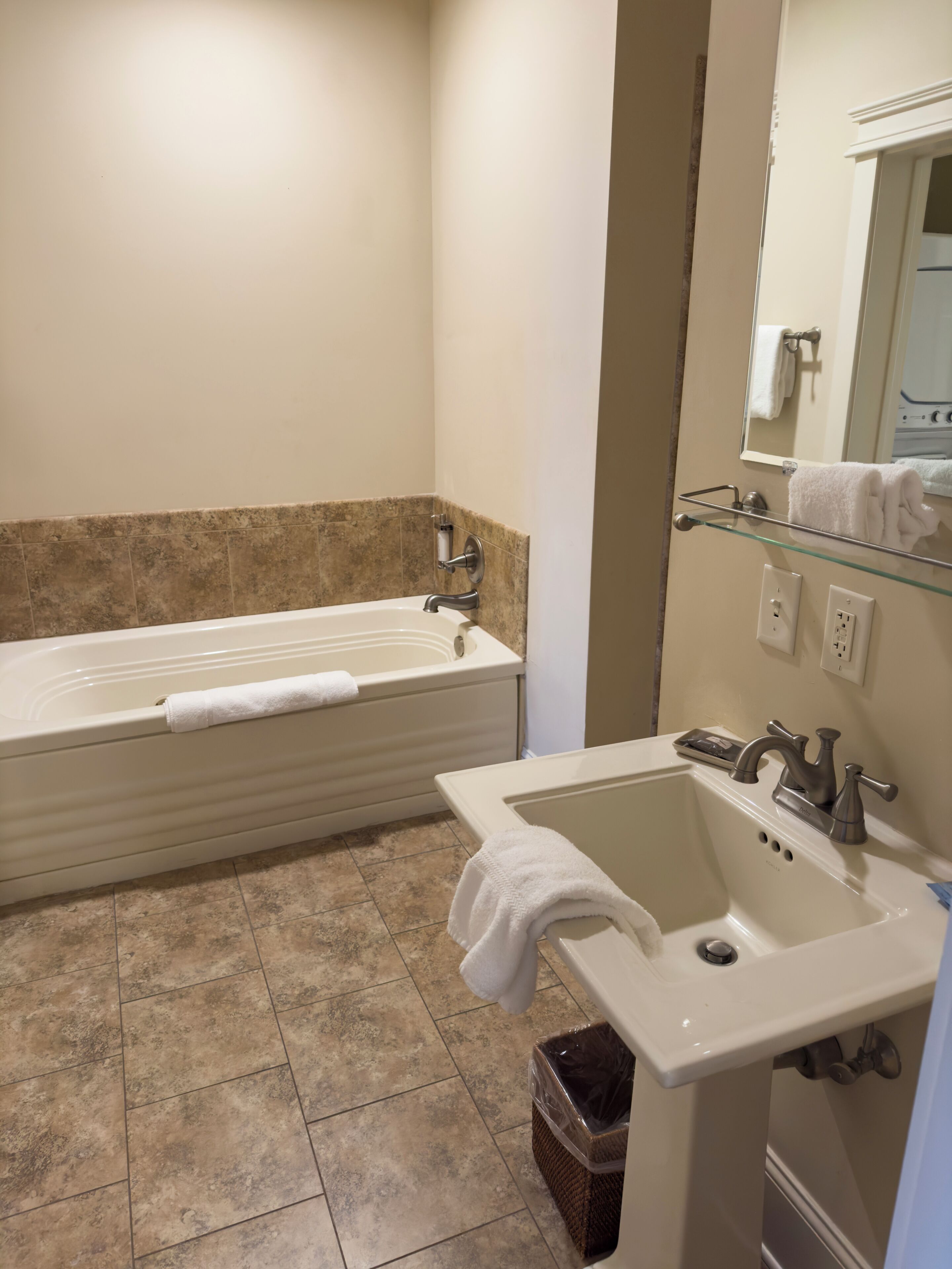 Une salle de bain avec une baignoire, un lavabo et une étagère en verre sur laquelle est posée une serviette.