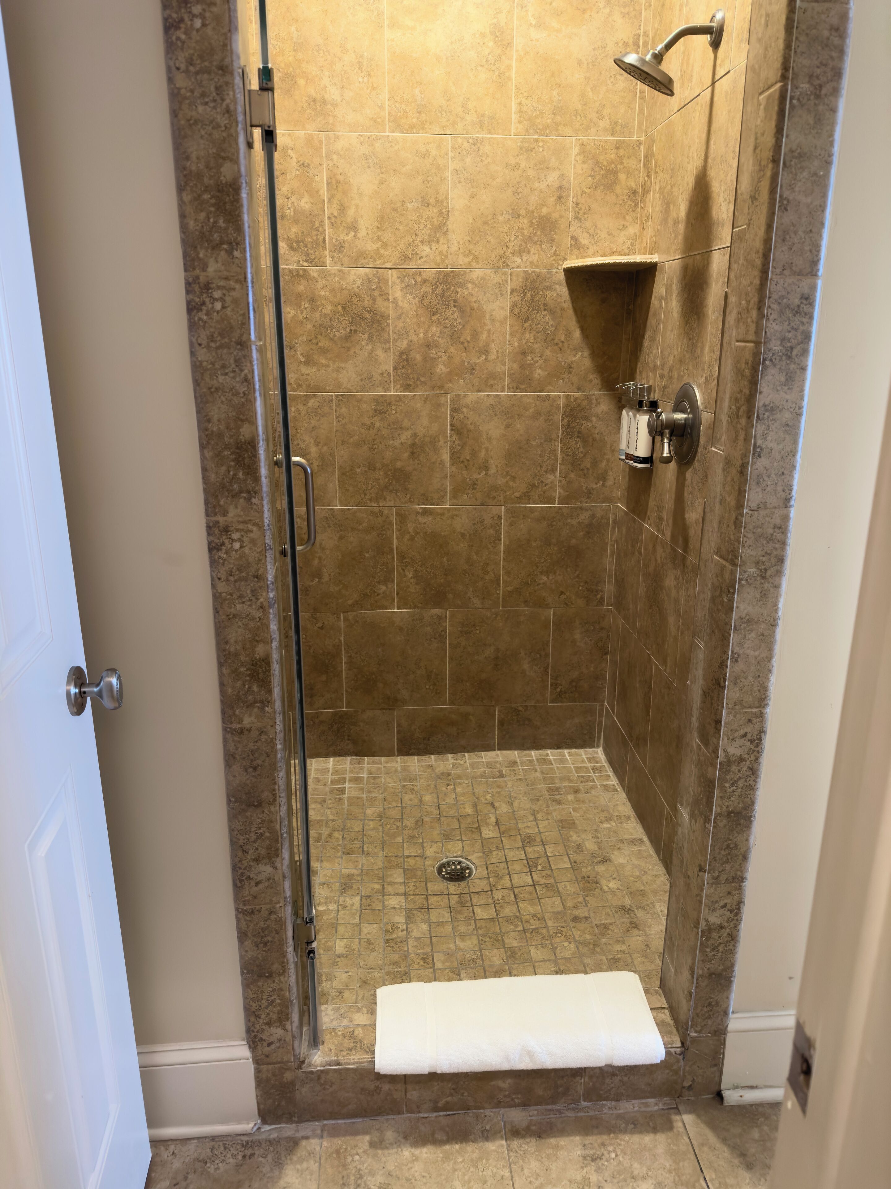 A walk-in shower with a glass door, a white towel on the floor, and a showerhead mounted on the wall.